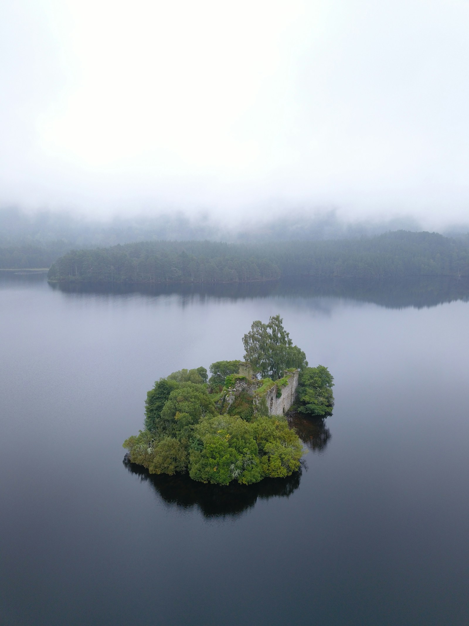 A quiet Scottish loch with a wooded island and distant mist